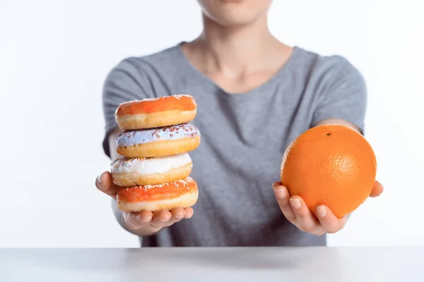 Cropped shot of girl holding ripe orange and sweet donuts — Stock Photo