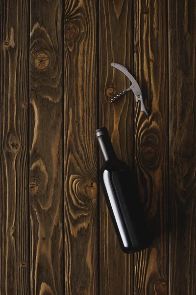 Top view of bottle of red wine and corkscrew on wooden table — Stock Photo