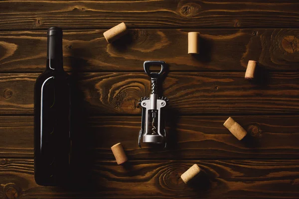 Top view of bottle of luxury red wine with corkscrew surrounded with corks on wooden table — Stock Photo