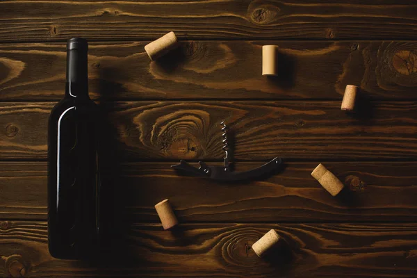 Vue du dessus de la bouteille de vin rouge avec tire-bouchon entouré de bouchons sur une table en bois — Photo de stock