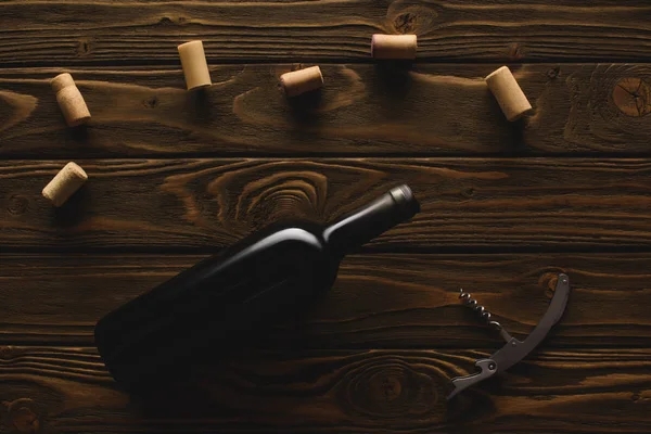 Top view of bottle of red wine with corks and corkscrew on wooden table — Stock Photo