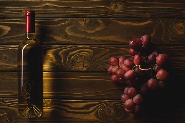 Vue de dessus de bouteille de vin blanc et branche de raisin sur table en bois — Photo de stock