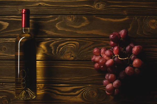 Top view of bottle of white wine and branch of grapes on wooden table — Stock Photo