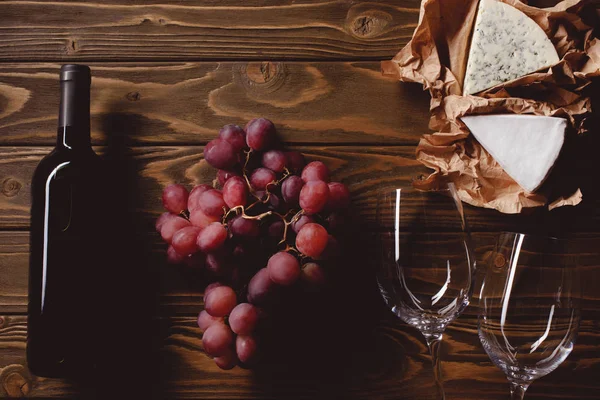 Vista superior de garrafa de vinho tinto com copos e aperitivos em mesa de madeira — Fotografia de Stock