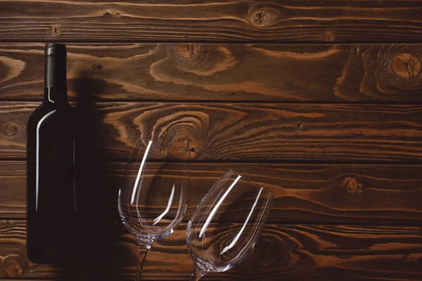 Vista superior de garrafa de vinho tinto com copos vazios na mesa de madeira — Fotografia de Stock