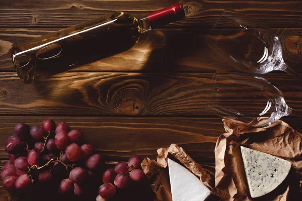 Vista superior de garrafa de vinho branco com copos e aperitivos em mesa de madeira — Fotografia de Stock