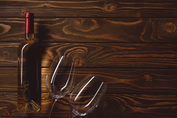 Vue du dessus de la bouteille de vin blanc avec des verres vides sur une table en bois — Photo de stock