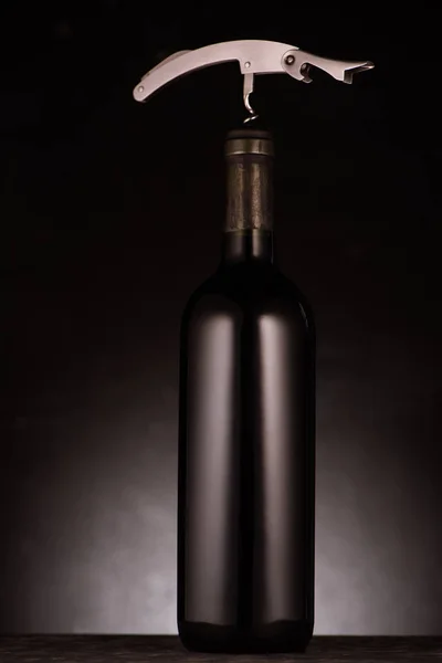 Bottle of red wine pierced with corkscrew on black — Stock Photo