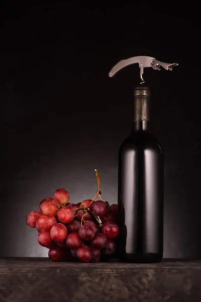 Flasche Rotwein durchbohrt mit Korkenzieher und Trauben auf schwarz — Stockfoto