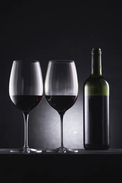 Glasses filled with red wine and wine bottle on black — Stock Photo
