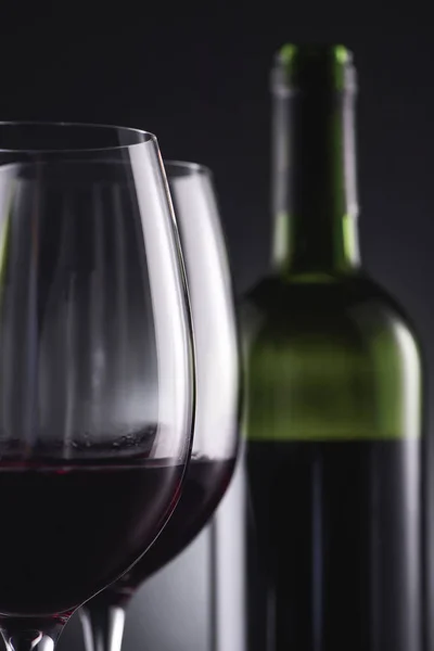 Close-up shot of glasses filled with red wine and wine bottle blurred on background — Stock Photo