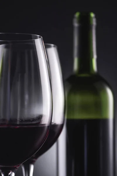 Close-up de copos cheios de vinho tinto e garrafa de vinho borrada no fundo — Fotografia de Stock