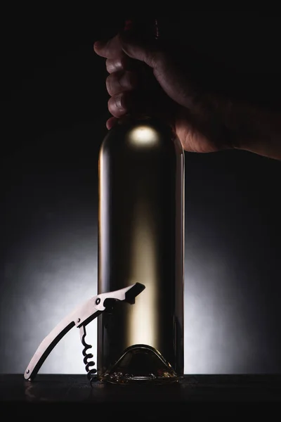 Cropped shot of man holding bottle of white wine on black with corkscrew — Stock Photo