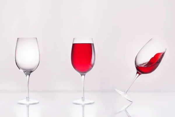 Vino vacío con lleno e inclinado en fila sobre superficie reflectante y sobre blanco - foto de stock