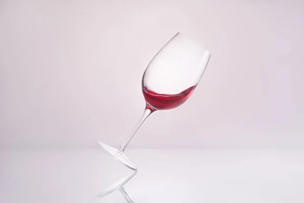 Schräges Weinglas mit spritzendem Luxus-Rotwein auf reflektierender Oberfläche und auf weißem — Stockfoto