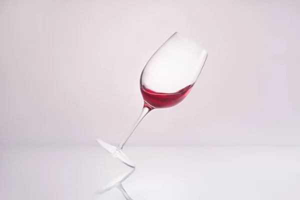 Inclined wineglass with splashing luxury red wine on reflective surface and on white — Stock Photo