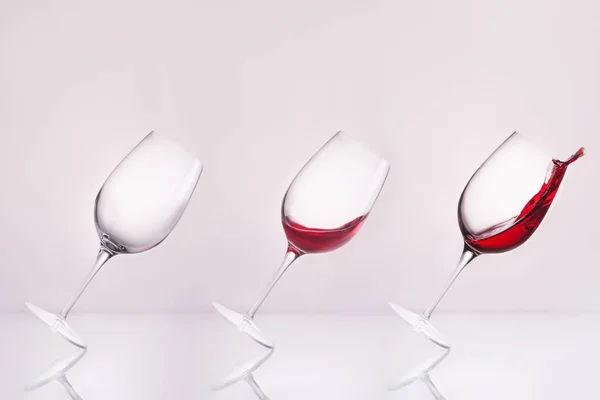 Row of inclined wineglasses empty and with splashing wine on reflective surface and on white — Stock Photo