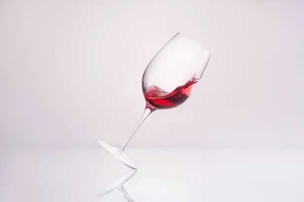 Verre incliné avec éclaboussures de vin rouge sur la surface réfléchissante et sur blanc — Photo de stock