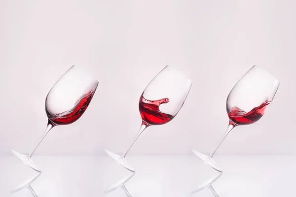 Rangée de verres à vin inclinés avec éclaboussures de vin sur la surface réfléchissante et sur blanc — Photo de stock