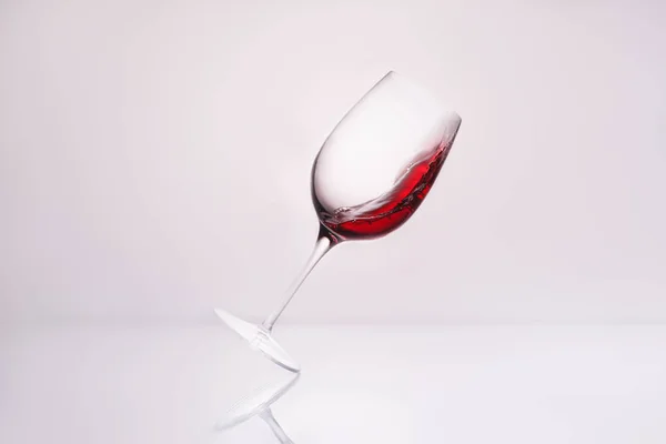 Inclined wineglass with red wine on reflective surface and on white — Stock Photo