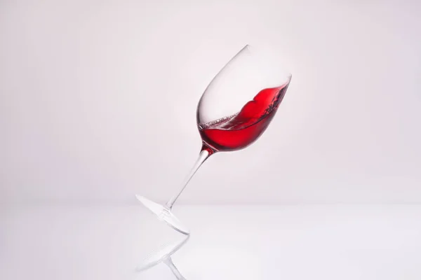 Primer plano de vino inclinado con vino tinto salpicado en superficie reflectante y en blanco - foto de stock