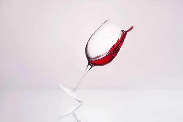 Vinho inclinado com vinho tinto de luxo na superfície reflexiva e no branco — Fotografia de Stock