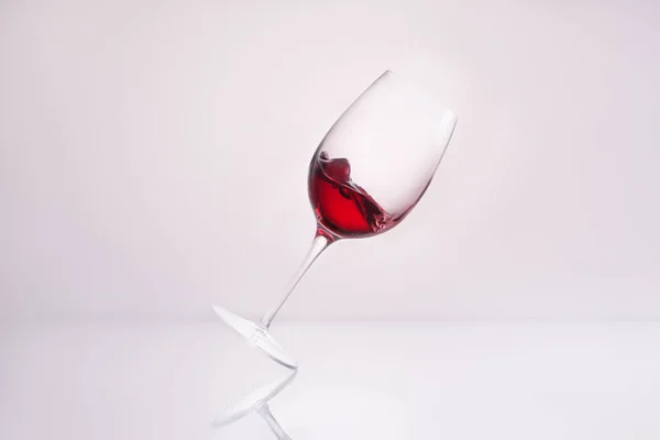 Vidro inclinado com vinho tinto na superfície reflexiva e no branco — Fotografia de Stock