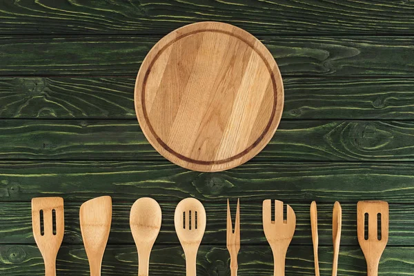 Vista dall'alto del tagliere rotondo e degli utensili da cucina disposti in fila sul tavolo di legno — Foto stock