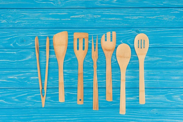 Верхний вид деревянной кухонной утвари, расположенной в ряд на голубом столе — стоковое фото