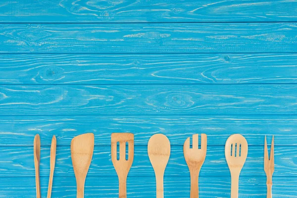 Vista superior de utensilios de cocina de madera colocados en fila en la mesa azul - foto de stock