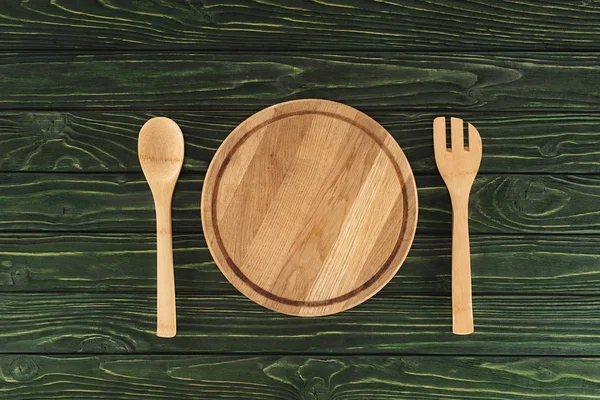 Vue du dessus de la planche à découper ronde entre la fourchette et la cuillère sur une table en bois — Photo de stock