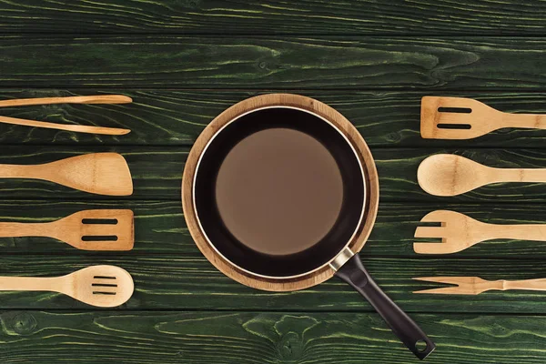 Top view of frying pan on round cutting board between wooden kitchen utensils on table — Stock Photo