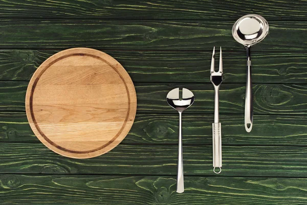 Top view of round wooden cutting board and metallic kitchen utensils on table — Stock Photo