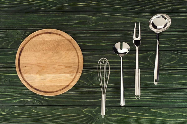 Vista superior de tabla de cortar de madera redonda y utensilios de cocina metálicos en la mesa - foto de stock