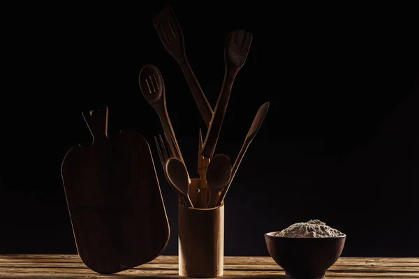 Tazón con harina y tabla de cortar con utensilios de cocina sobre fondo negro - foto de stock