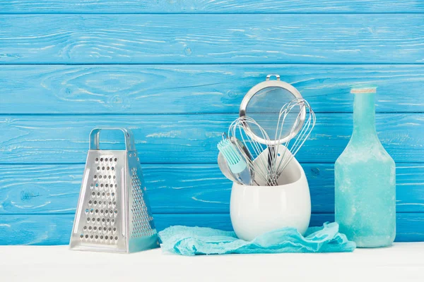 Closeup view of rag, bottle, pastry brush, grater, whisks and sieve in front of blue wooden wall — Stock Photo