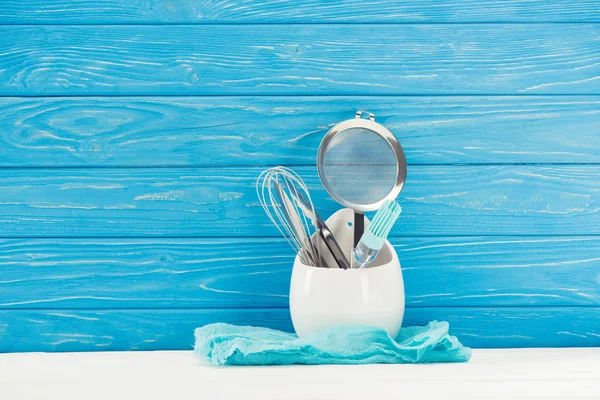 Closeup shot of rag, pastry brush, whisk and sieve in front of blue wooden wall — Stock Photo
