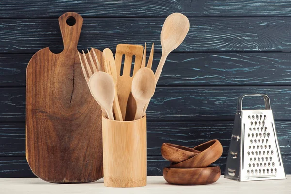 Gros plan de planche à découper, ustensiles de cuisine, râpe et ramequins devant un mur en bois — Photo de stock