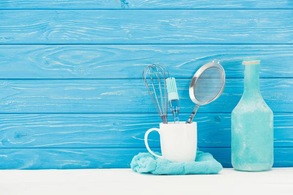 Nahaufnahme von Lappen, Schneebesen, Sieb, Teigpinsel und Flasche vor der Holzwand — Stockfoto