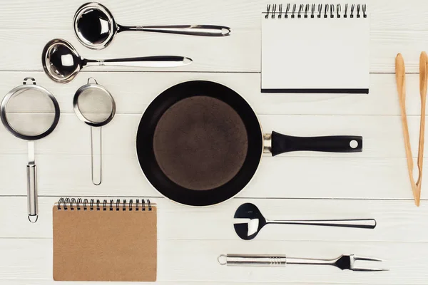 Vue du dessus des manuels scolaires, poêle à frire et ustensiles de cuisine sur table en bois blanc — Photo de stock