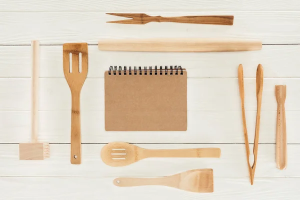 Vue du dessus du manuel et des ustensiles de cuisine en bois sur la table blanche — Photo de stock