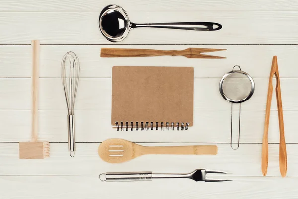 Elevated view of textbook and kitchen utensils on wooden white table — Stock Photo