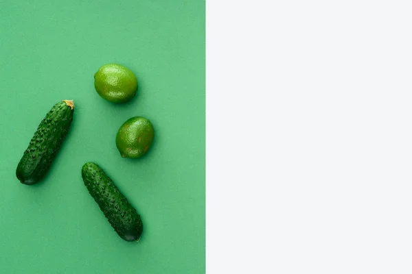 Top view of limes and cucumbers on white and green surface — Stock Photo