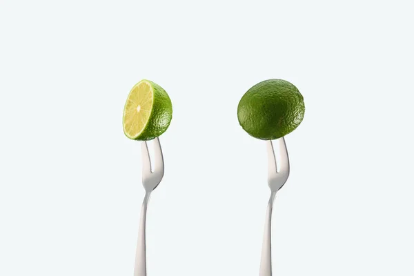 Lime intere e tagliate su forchette isolate su bianco — Foto stock