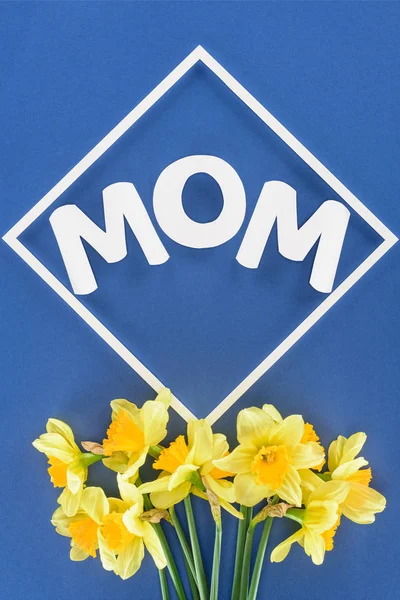 Top view of bouquet of daffodils and word mom in frame isolated on blue, mothers day concept — Stock Photo