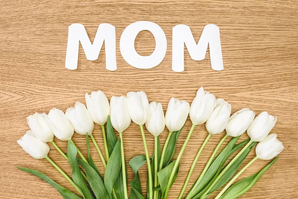 Top view of white tulips and word mom on wooden table, mothers day concept — Stock Photo