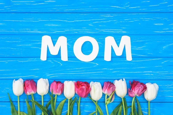 Top view of pink and white tulips and word mom on blue table, mothers day concept — Stock Photo