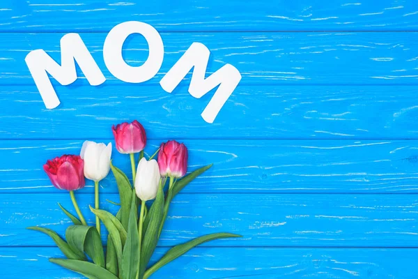 Top view of bouquet of pink and white tulips and word mom on blue table, mothers day concept — Stock Photo
