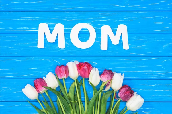 Elevated view of bouquet of pink and white tulips and word mom on blue table, mothers day concept — Stock Photo
