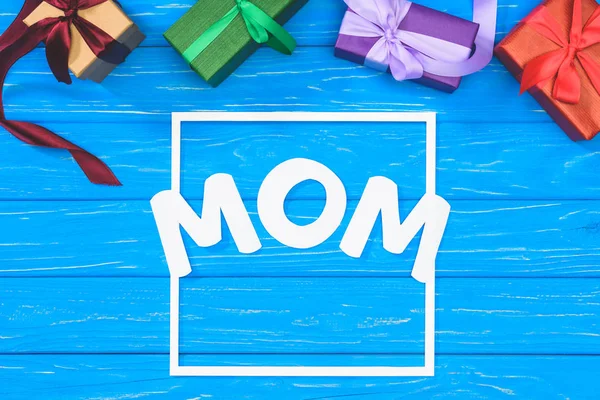 Top view of gift boxes and word mom in frame on blue table, mothers day concept — Stock Photo